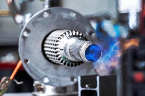 Ein silberner Brennermund mit blauer Ammoniakflamme in einer Industriehalle.