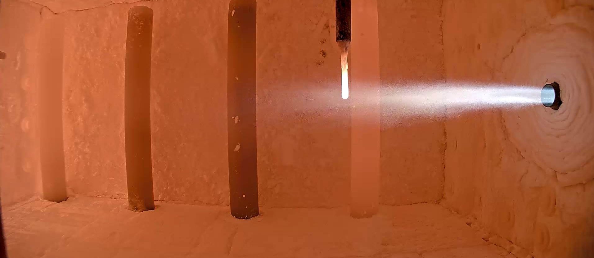 Das Bild zeigt eine Brennkammer mit laufendem Versuchsaufbau, in dem ein Ammoniakbrenner in Betrieb ist. Der Brennerstrahl tritt in die aufgeheizte Kammer ein und verdeutlicht die experimentelle Nutzung von Ammoniak (NH₃) als CO₂-freien Brennstoff. Diese Aufnahme steht für die Forschungsaktivitäten des GWI zur Dekarbonisierung energieintensiver Industrieprozesse mithilfe innovativer Brennstoffe.