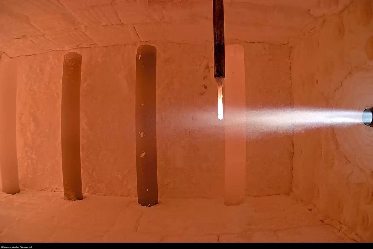 Das Bild zeigt eine Brennkammer mit laufendem Versuchsaufbau, in dem ein Ammoniakbrenner in Betrieb ist. Der Brennerstrahl tritt in die aufgeheizte Kammer ein und verdeutlicht die experimentelle Nutzung von Ammoniak (NH₃) als CO₂-freien Brennstoff. Diese Aufnahme steht für die Forschungsaktivitäten des GWI zur Dekarbonisierung energieintensiver Industrieprozesse mithilfe innovativer Brennstoffe.