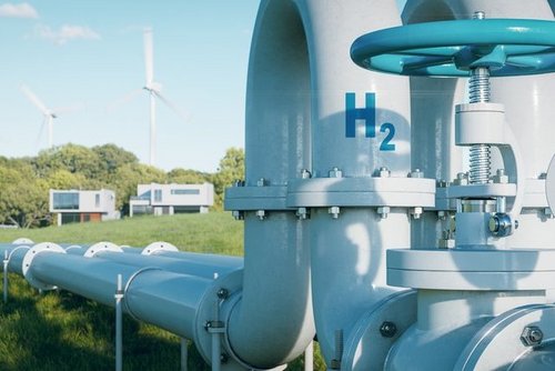 Das Bild zeigt ein Wasserstoff-Industrieventil mit Druckanzeige, beschriftet mit „H₂“. Im Hintergrund sind Windkraftanlagen sichtbar, die die Verbindung zwischen erneuerbaren Energien und Wasserstofftechnologien symbolisieren. Diese Darstellung verdeutlicht die Rolle von grünem Wasserstoff und erneuerbarem Gas als tragende Säule der Energiewende.