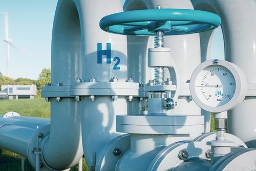 Das Bild zeigt ein Wasserstoff-Industrieventil mit Druckanzeige, beschriftet mit „H₂“. Im Hintergrund sind Windkraftanlagen sichtbar, die die Verbindung zwischen erneuerbaren Energien und Wasserstofftechnologien symbolisieren. Diese Darstellung verdeutlicht die Rolle von grünem Wasserstoff und erneuerbarem Gas als tragende Säule der Energiewende.