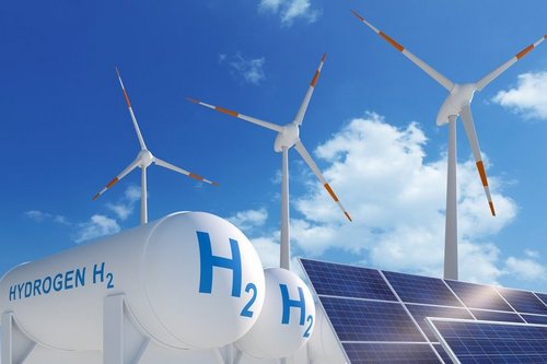 Das Bild zeigt große Wasserstofftanks (H₂) im Vordergrund, flankiert von Windkraftanlagen und einem Solarmodul. Diese Komposition symbolisiert die Verknüpfung erneuerbarer Energien mit der Wasserstofftechnologie und verdeutlicht deren zentrale Rolle in der Energiewende.